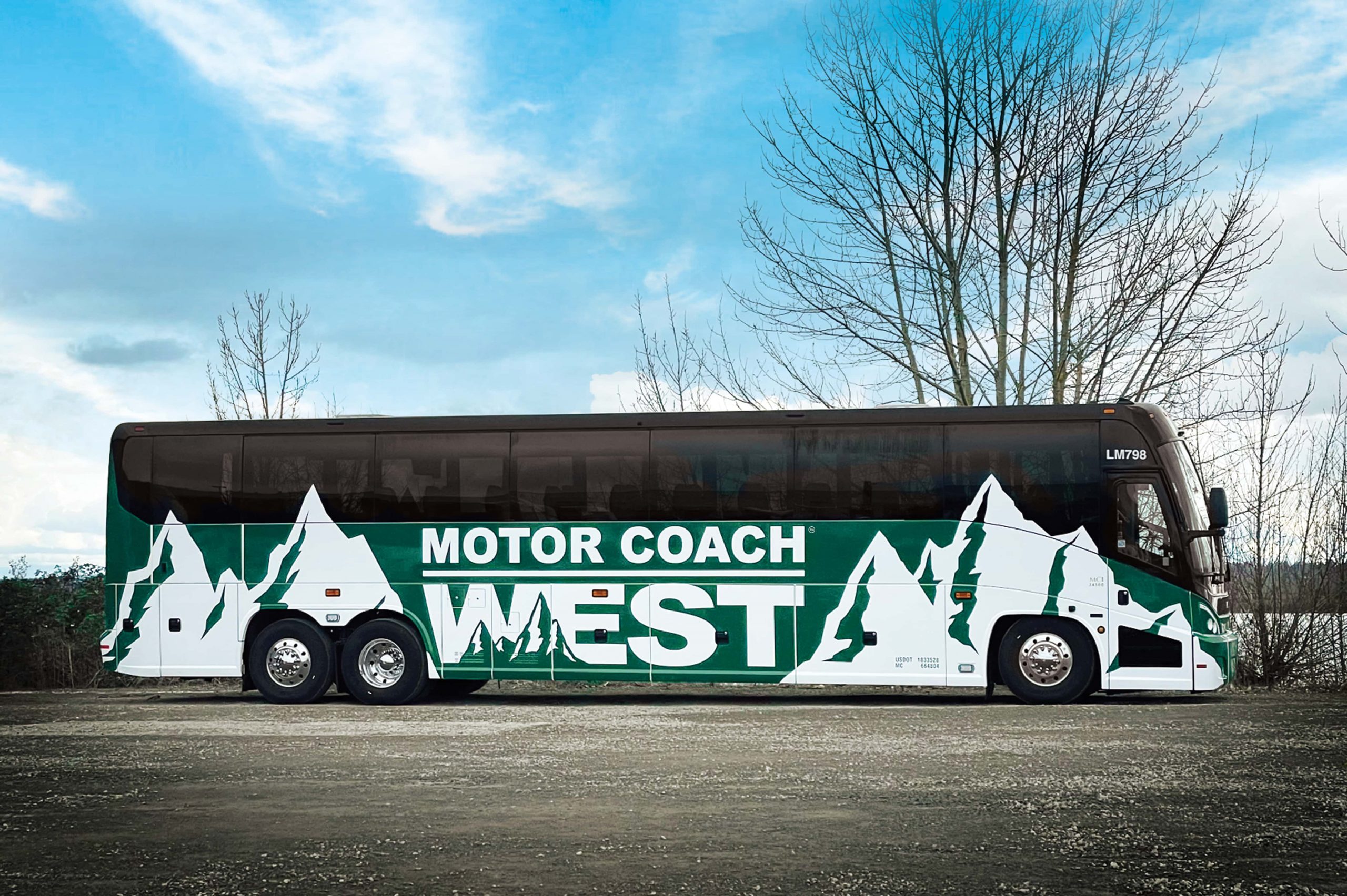Green Motor Coach West bus against partly cloudy sky background.