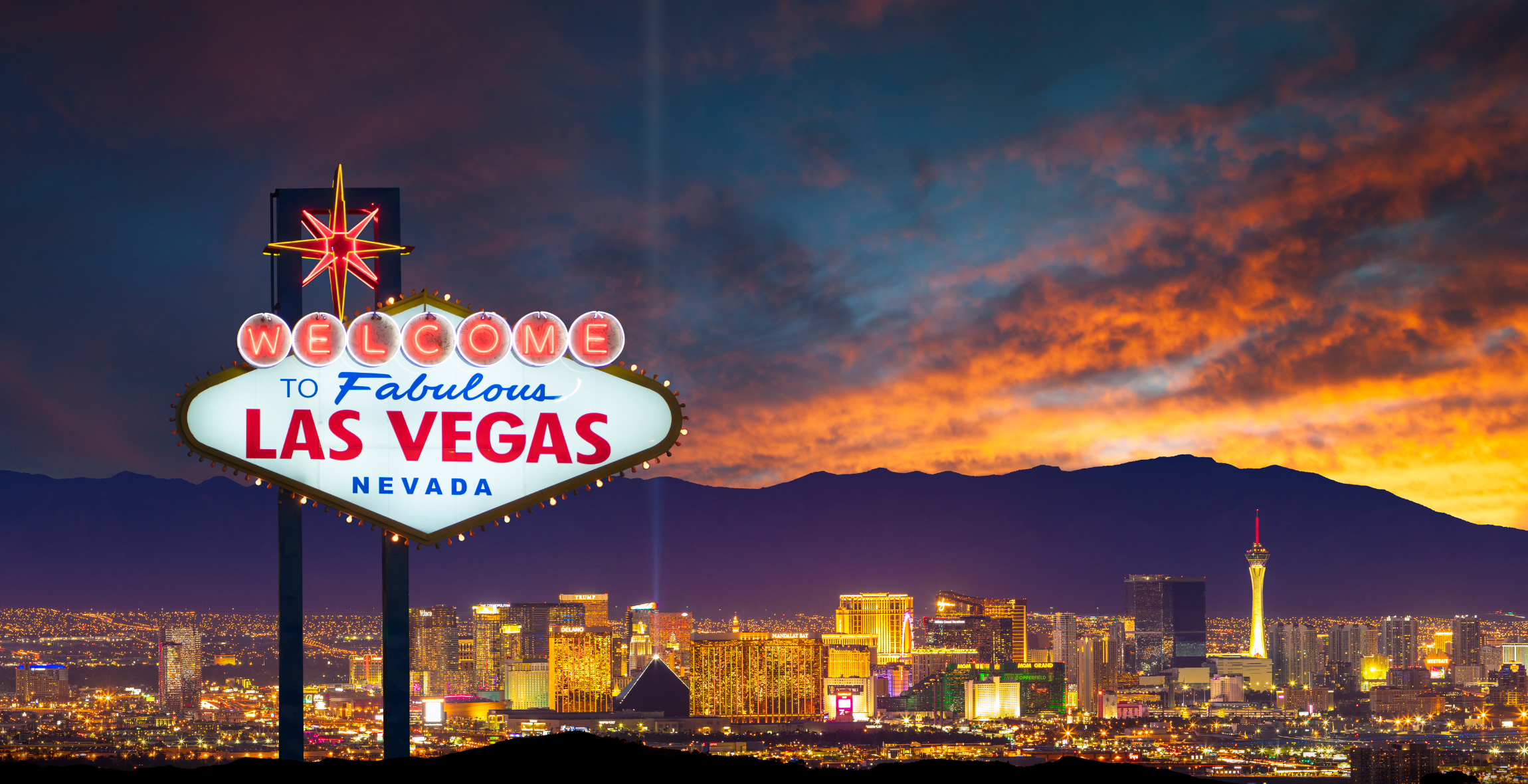  'Welcome to Fabulous Nevada' Sign is in front of a sunset and mountain and city