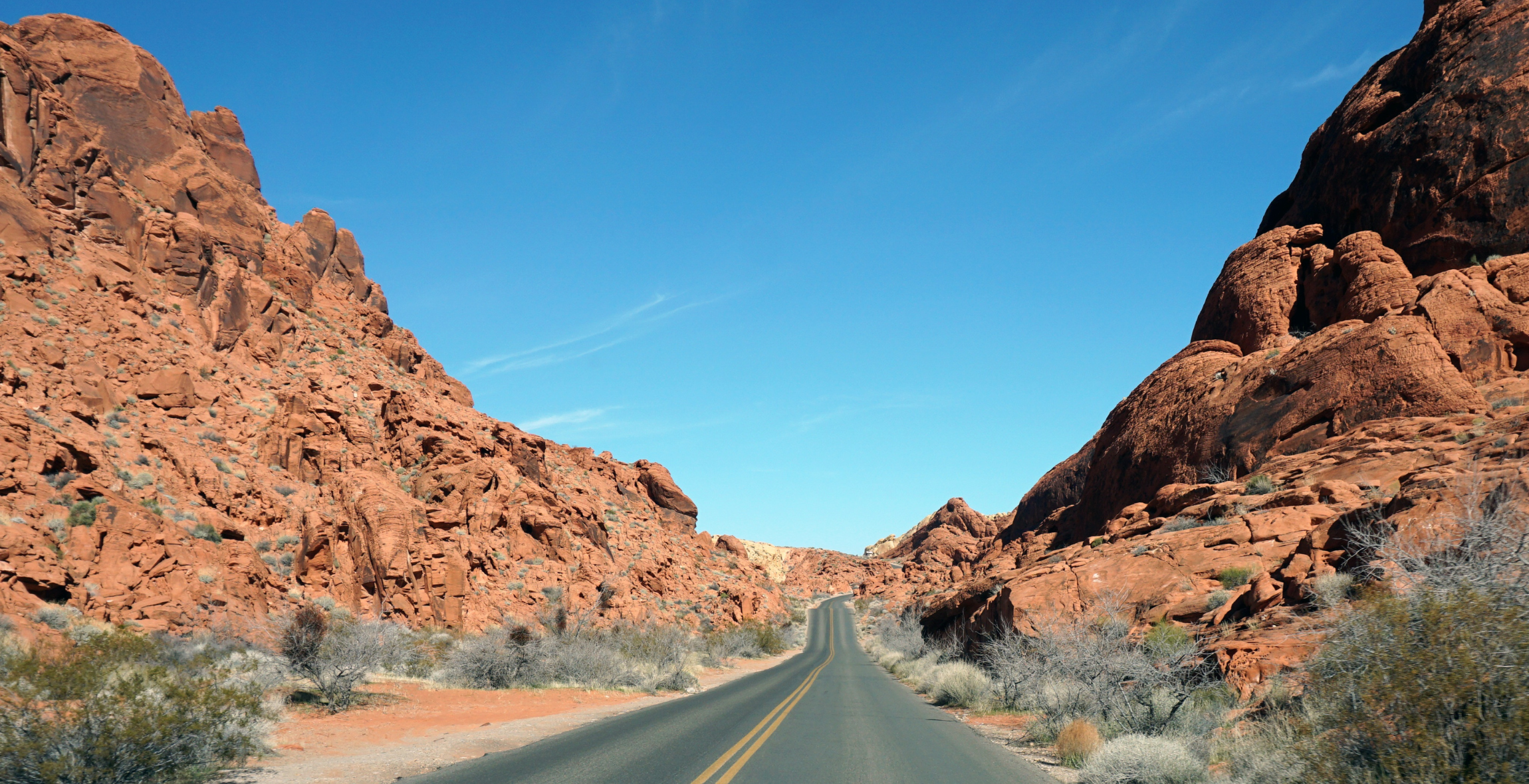an empty road is surrounded by red rocks and cliffs
